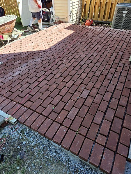 Mason laying red brick pavers on a compacted base for a new patio