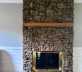 Finished floor-to-ceiling stone veneer fireplace with a timber mantel