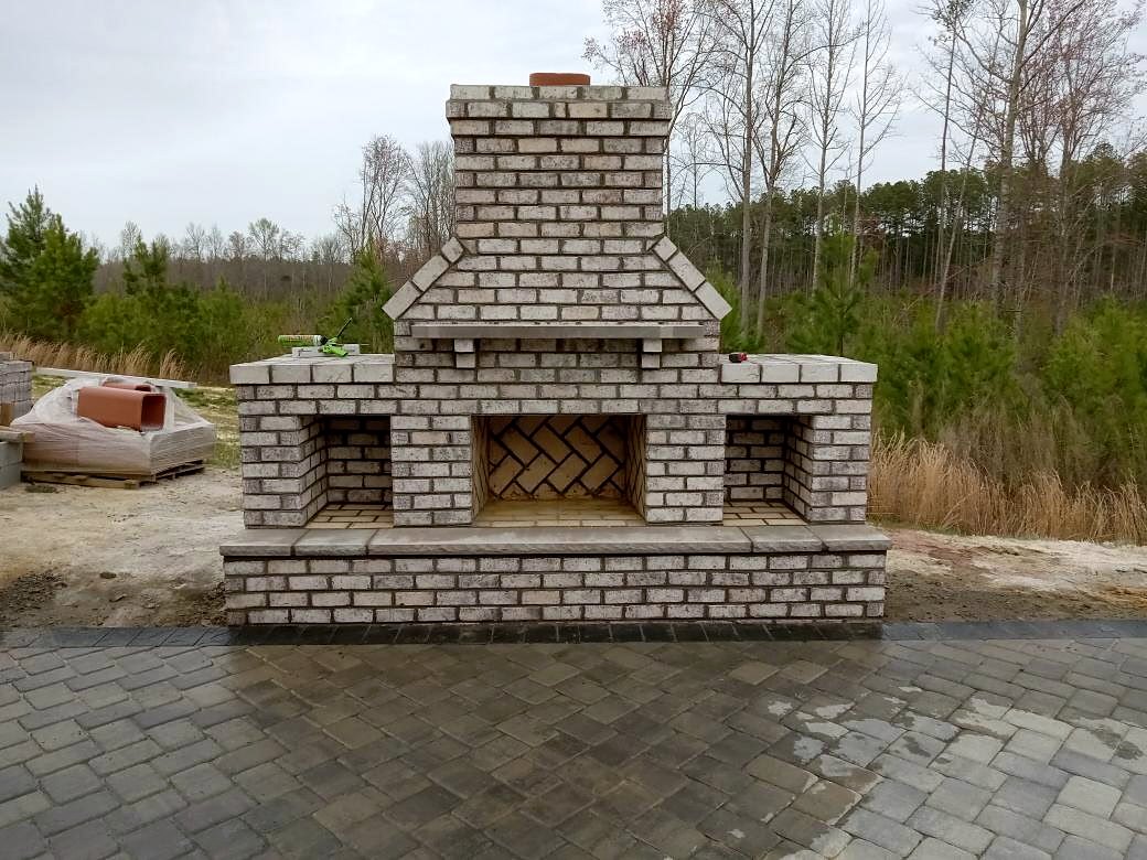 Finished light brick outdoor fireplace with herringbone firebox and two wood storage bays