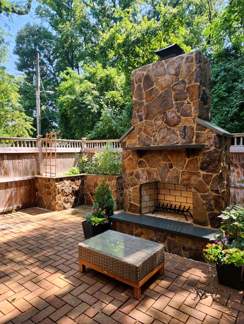 Tall fieldstone outdoor fireplace and seating wall in a private brick courtyard