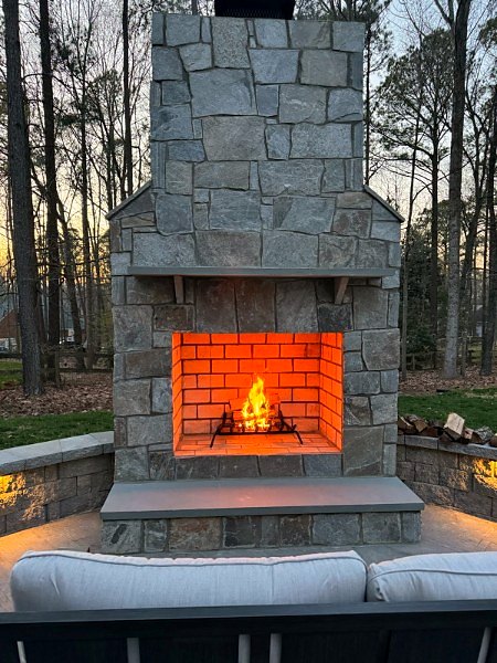Custom stone outdoor fireplace with a fire burning at dusk, Richmond VA